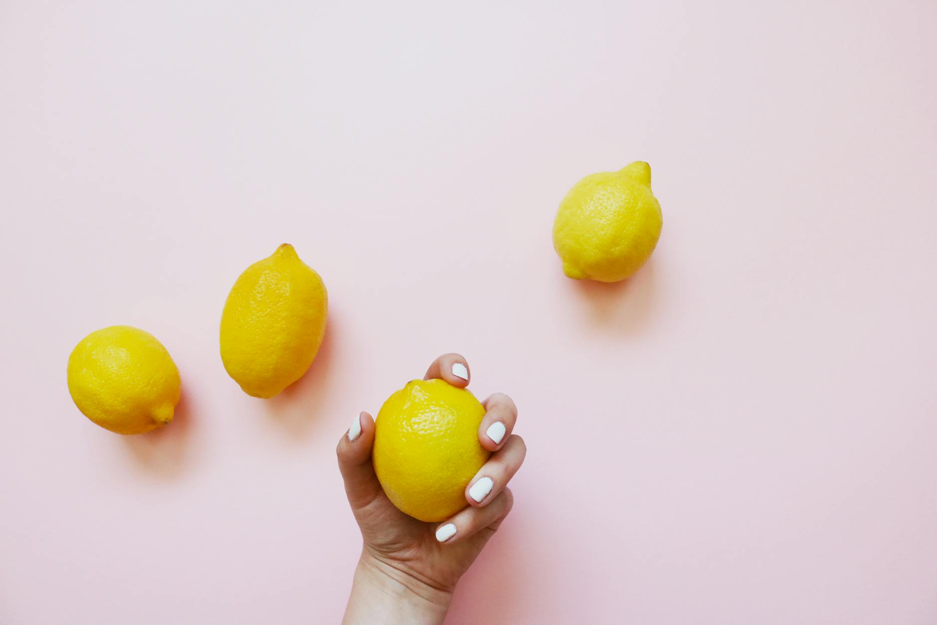 A hand holding a fresh lemon on a soft pink background, symbolizing returning to natural pleasure