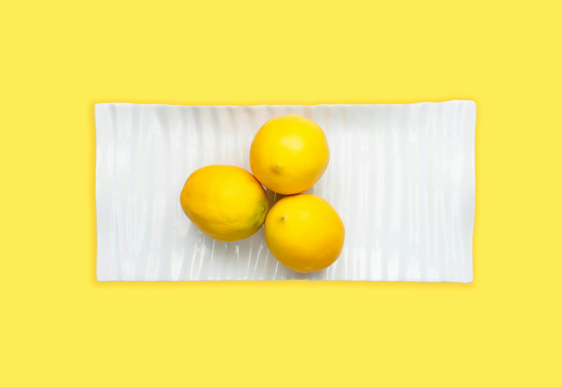 Fresh lemons arranged on white plate against vibrant yellow background