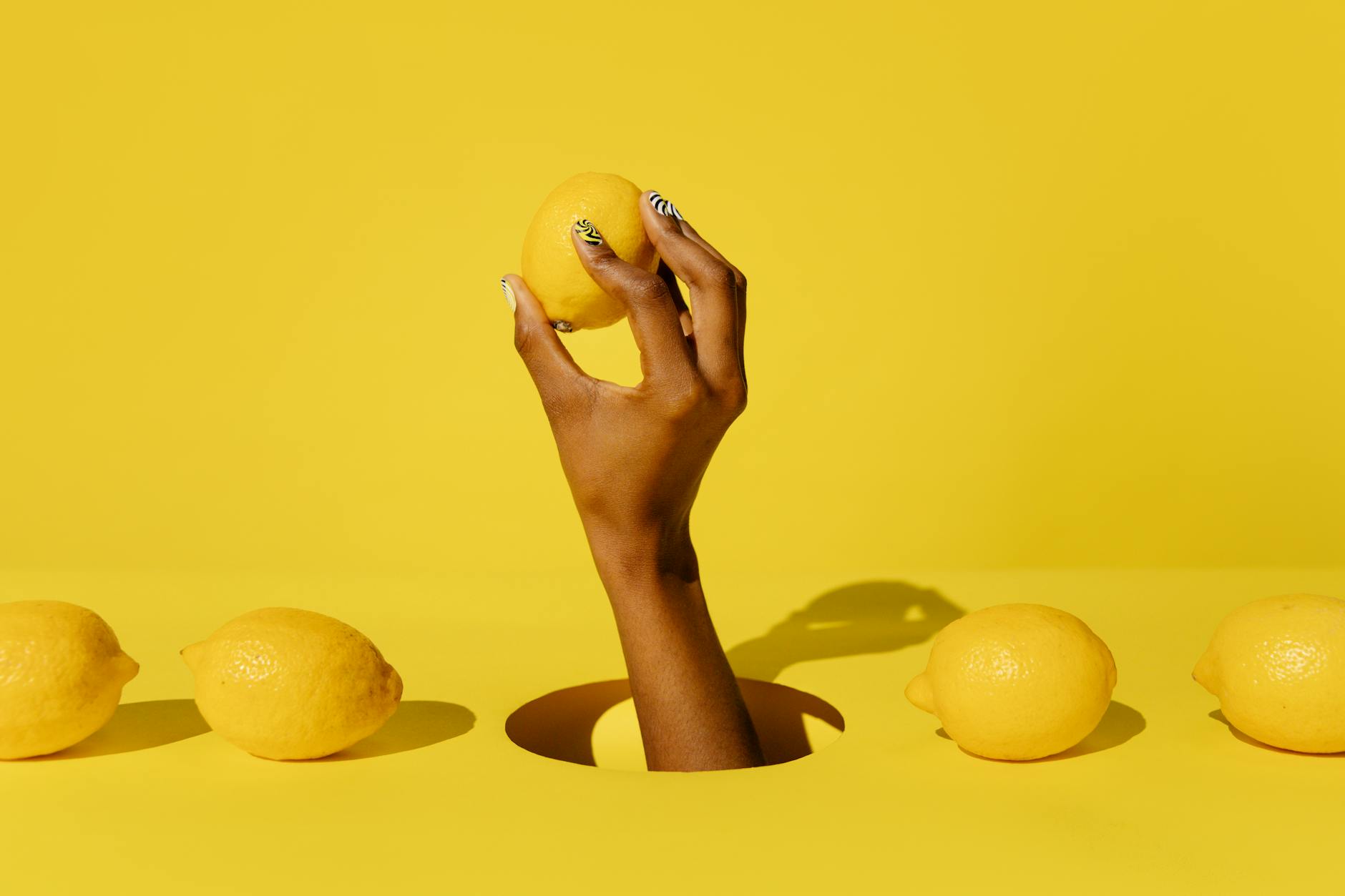 A hand holding a fresh lemon against a bright yellow background, symbolizing the renewal of pleasure and desire